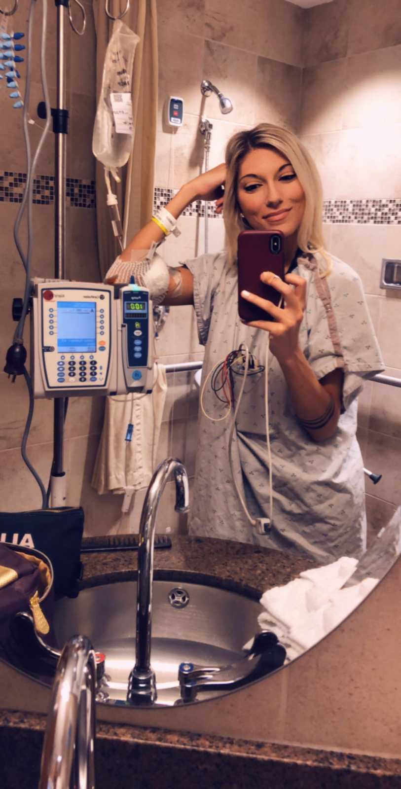 Woman with Superior Mesenteric Artery Syndrome standing smiling in selfie in hospital bathroom