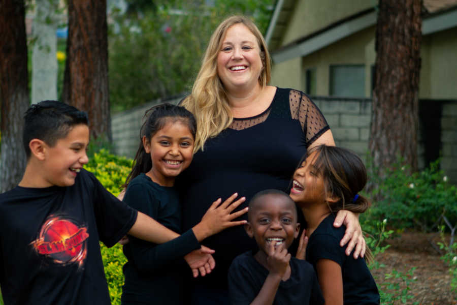 Pregnant foster mother smiles as with foster kids who smile and touch her stomach