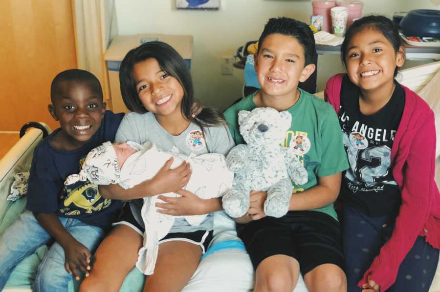 Foster kids sits on hospital bed holding foster mothers newborn