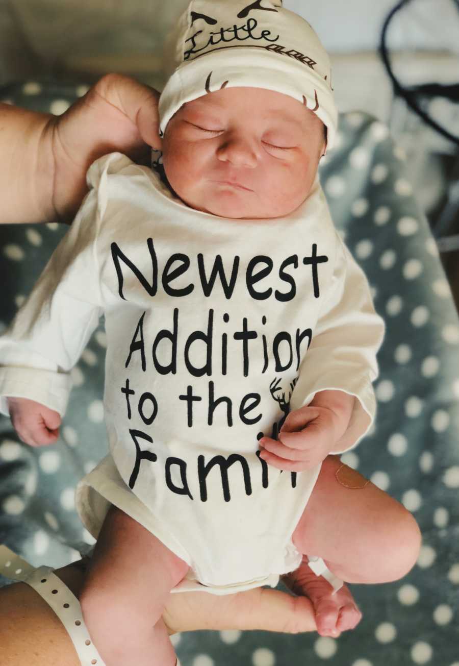 Foster mothers newborn wearing onesie saying, "Newest addition to the family"