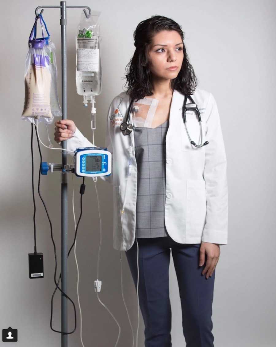 Woman with malformation who is now a doctor stands next to IV that is connected to her