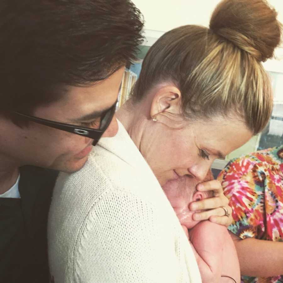 Woman holds newborn who was abandoned by mother close to her chest with husband behind her