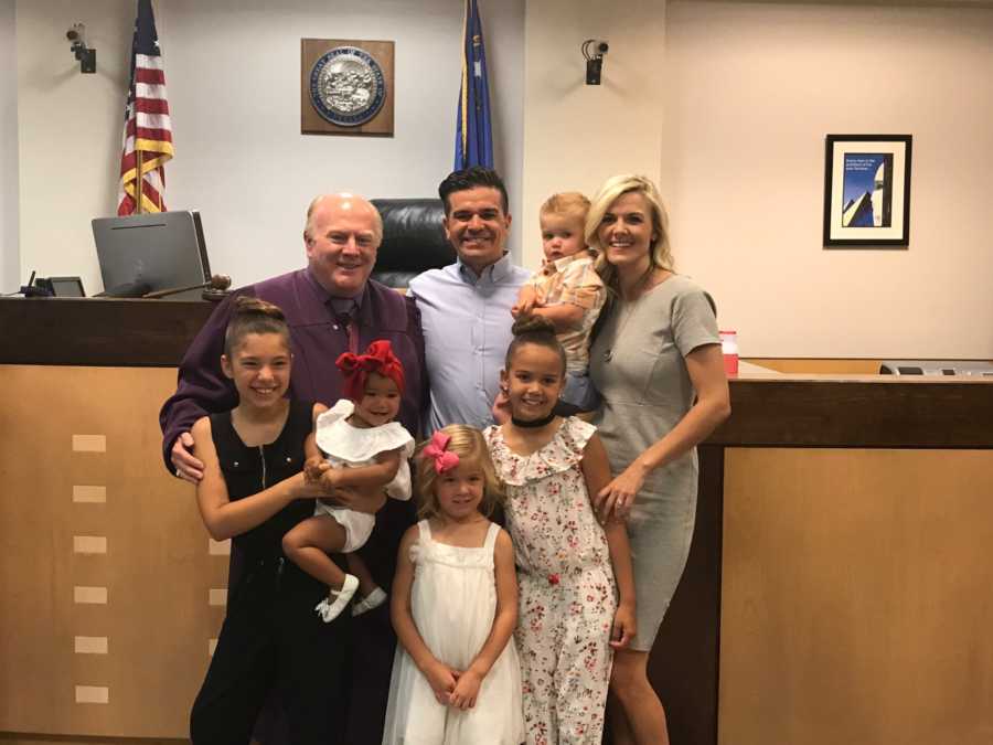 Mother and father standing with their four birth children and adopted baby boy in adoption court