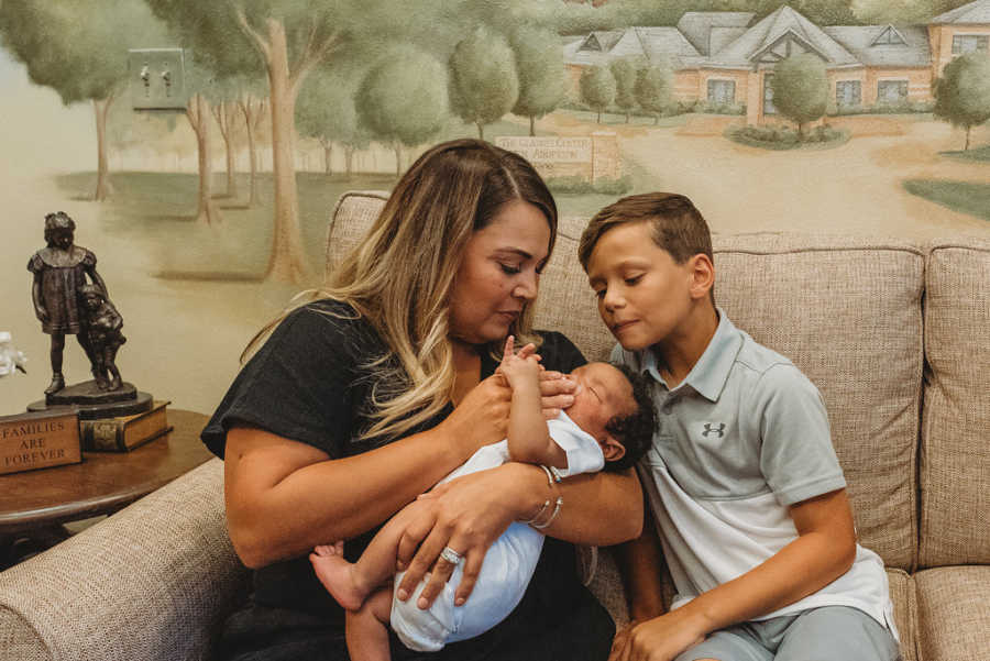 Foster mom puts pacifier in foster son's mouth while her biological son watches