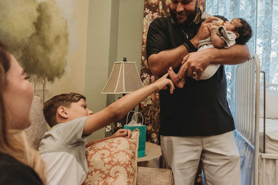 Biological son touches newborn foster child's feet while his dad holds him