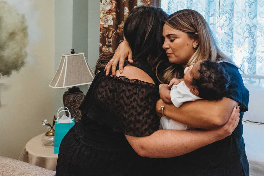 Foster mom hugs biological mom while they hold their shared son together