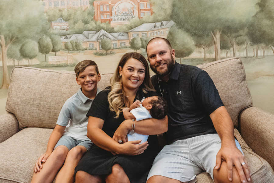 Family of four take photo together on a brown couch while meeting their foster son for the first time
