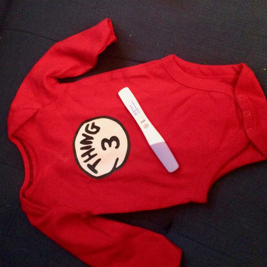 Red onesie that says, "Thing 3" with pregnancy test indicating woman is pregnant