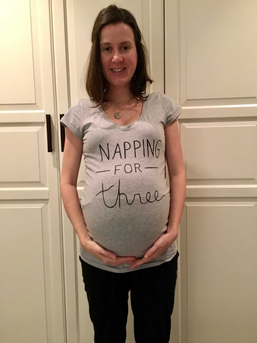 Woman who struggled with fertility stands holding stomach wearing t-shirt that says, "Napping for three"
