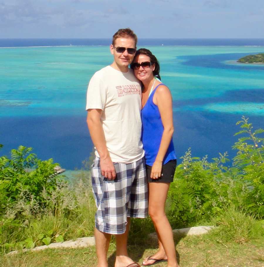 Husband and wife stand smiling on honeymoon in Tahiti with ocean in background