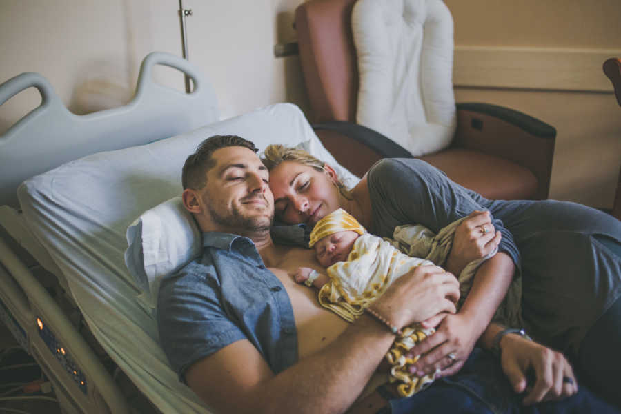 Husband and wife lay in hospital bed with adopted newborn