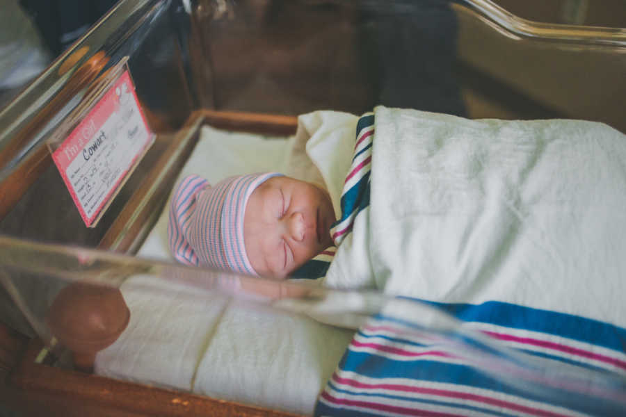 Adopted newborn sleeping in hospital swaddle in blanket with pink and blue hat on