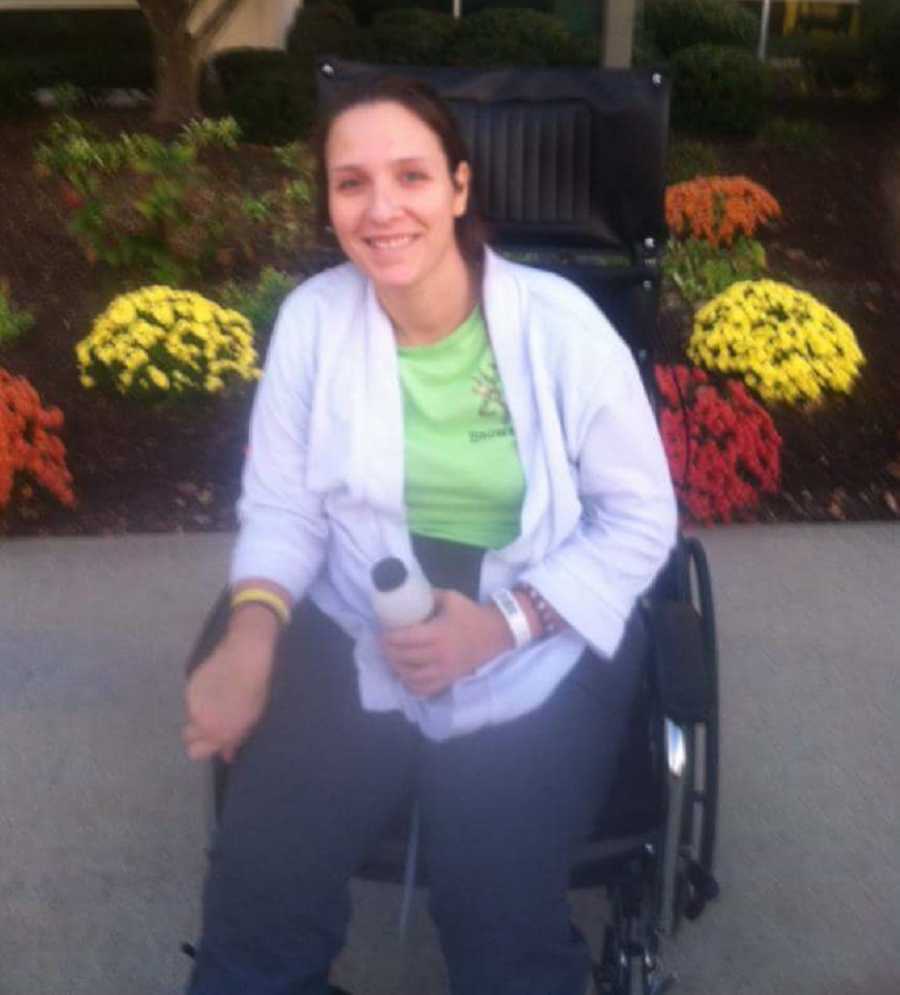 Young woman who overdosed sits in wheelchair smiling in front of yellow and red flowers