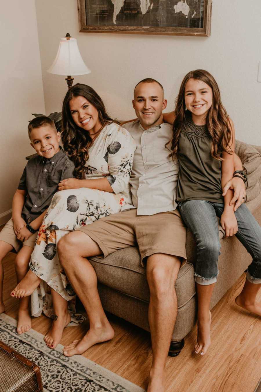 Family of four take a photo together while all sitting on the same chair together in similar green and brown colors