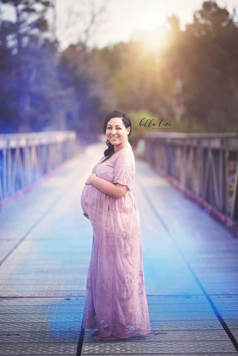 Woman pregnant with third child she struggled to have stands holding stomach on bridge