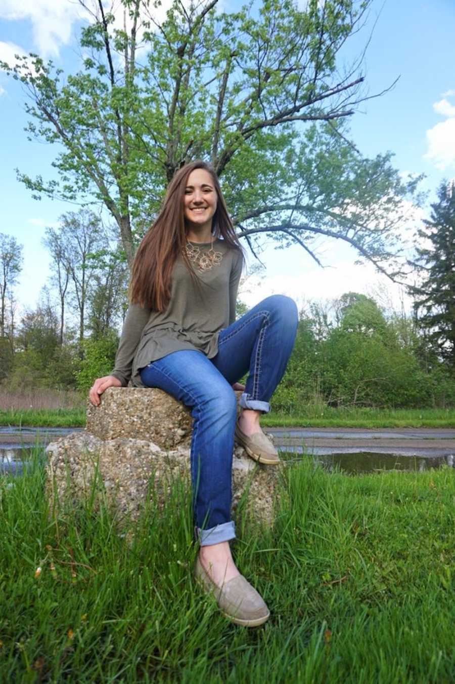 Teen who bought cup of coffee for random woman which meant a lot to her sits on rock smiling