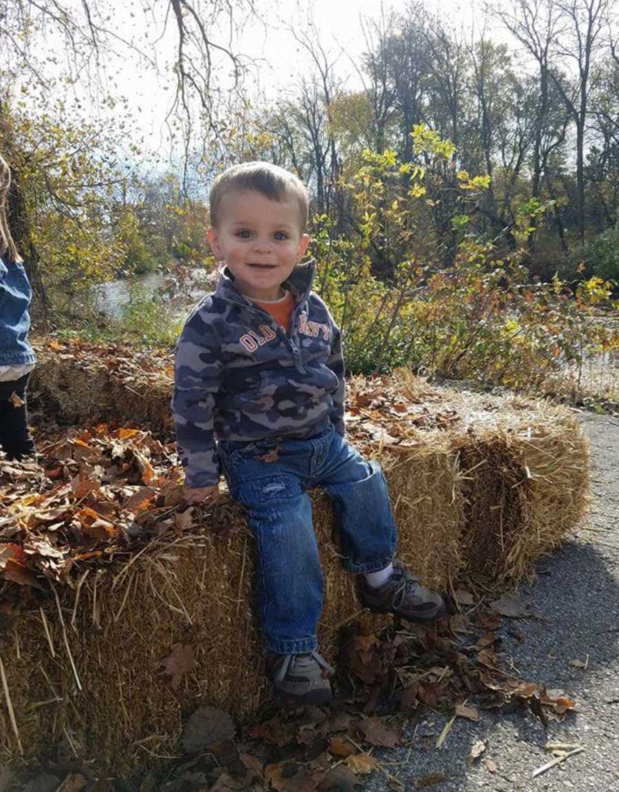 Little boy whose will have a tumor smiling while sitting on hay bale