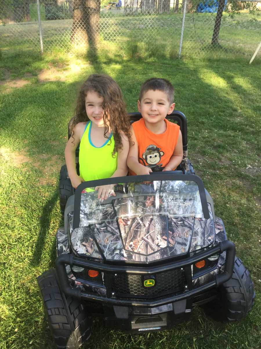 Toddler girl and adopted brother smile in toy john deer car
