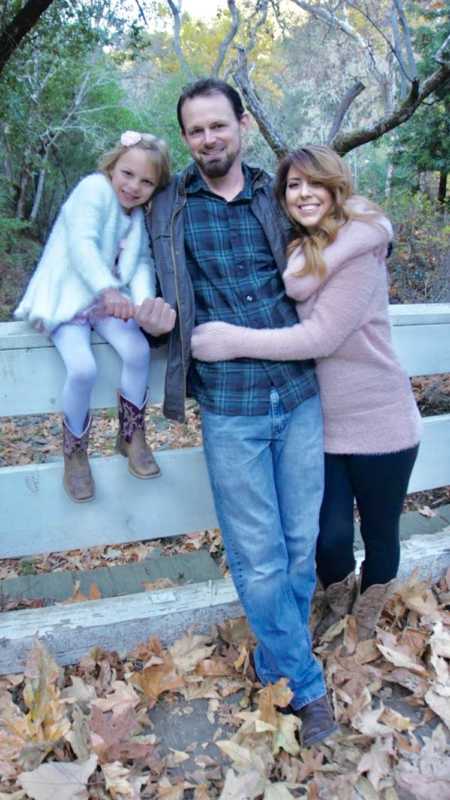 Family of three take fall-themed photos with green foliage behind them