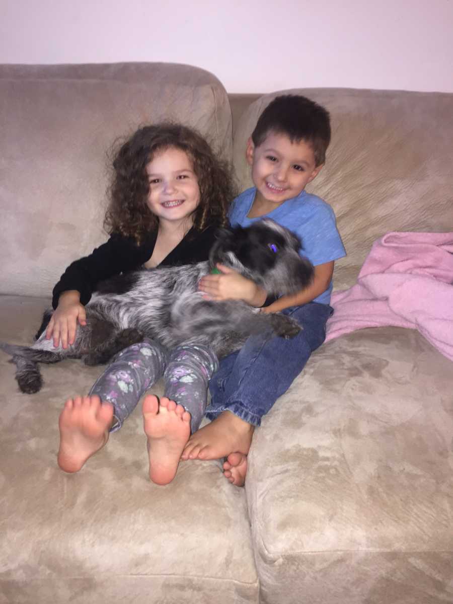 Little girl sits on couch next to adopted brother on couch with dog on their lap