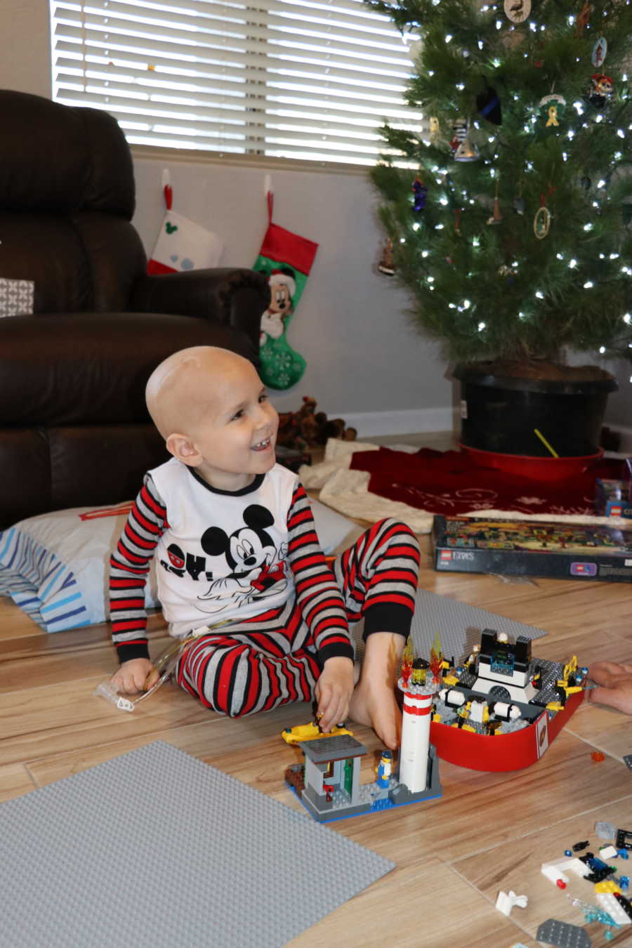 Little boy with brain cancer smiling on floor playing with legos on Christmas morning