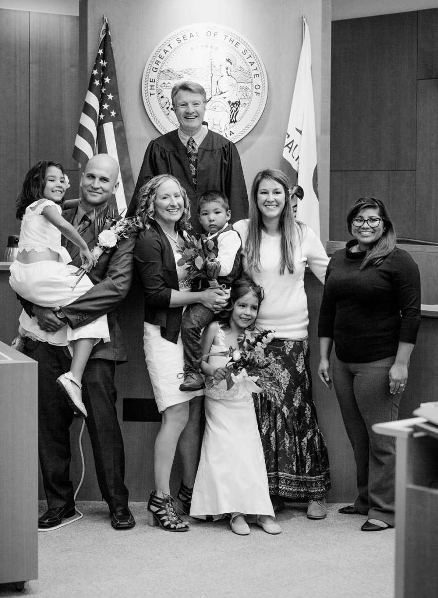 Husband and wife stand with their three adopted kids, judge, and two other woman at adoption court