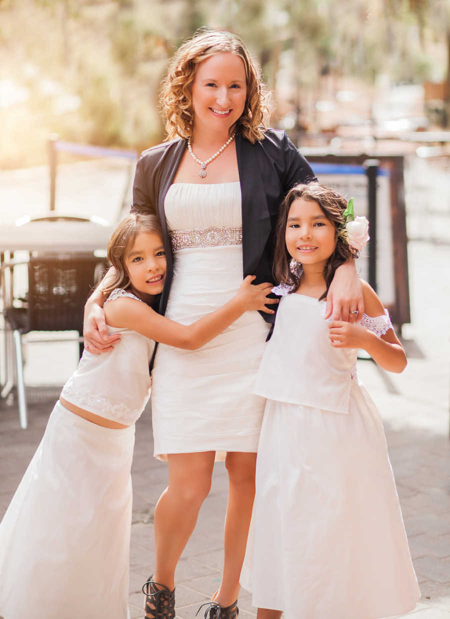 Mother stands with arms wrapped around two foster daughters who are dressed up for adoption