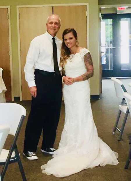 Bride with tattoos on arms stands smiling with father who surprised her with his own tattoo on wedding day