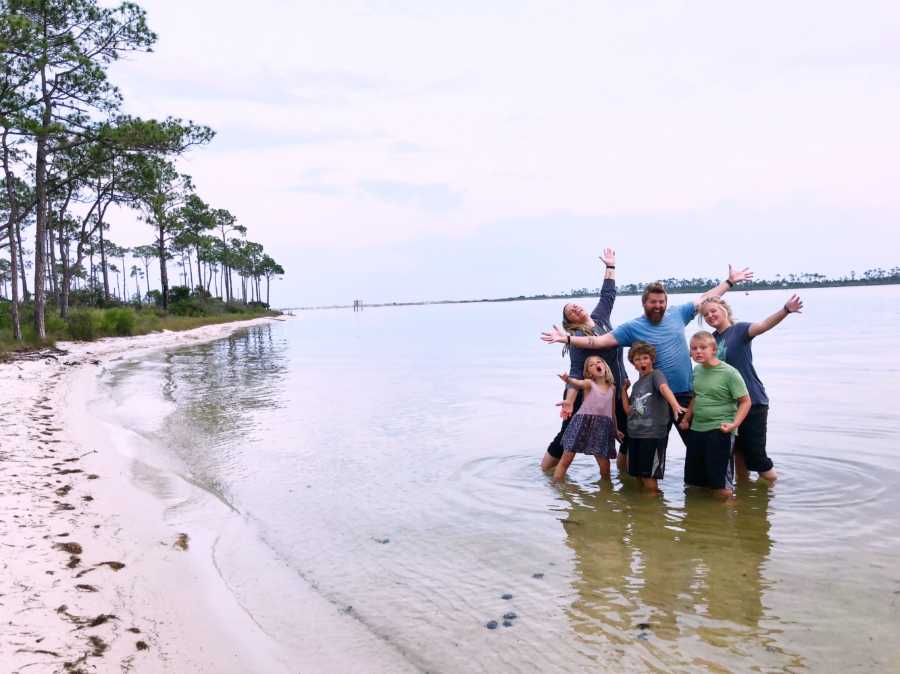 Family of six who travels the US in airstream stand posing in shallow body of water