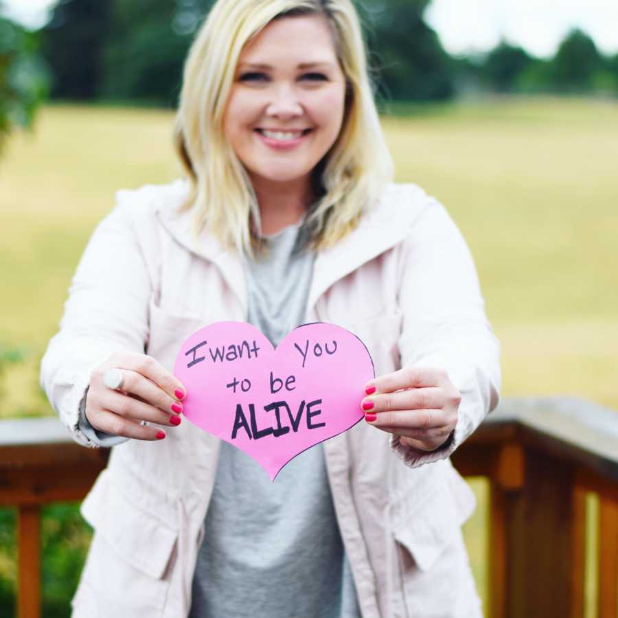 Woman who recovered from being closet drunk holds pink paper hearts that says, "I want you to be alive"
