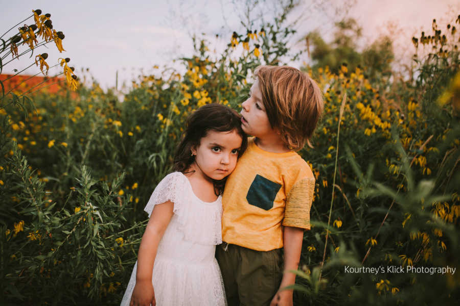 Boy with chromosome 7 inversion stands with arm around little sister in sunflower field
