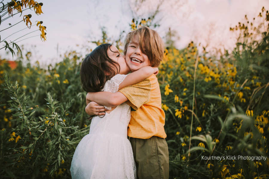 Boy with chromosome 7 inversion hugs little sister while she kisses him in sunflower field