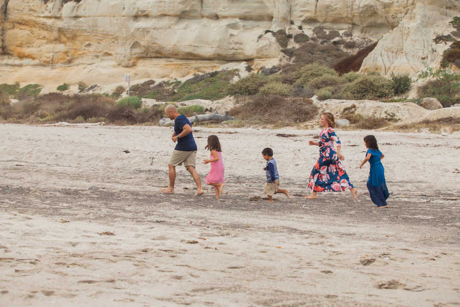 Mother and father walk in line with three adopted children on beach