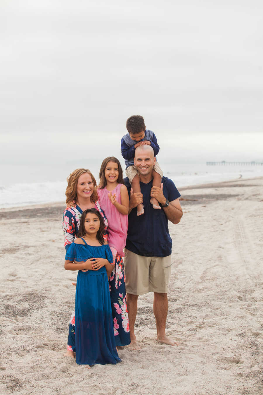 Father stands with adopted son on his shoulders beside wife and two adopted daughters