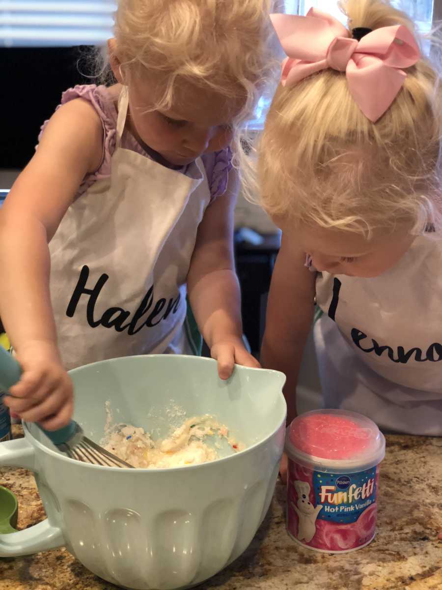 Little girl stirring cake batter in bowl with twin by her side