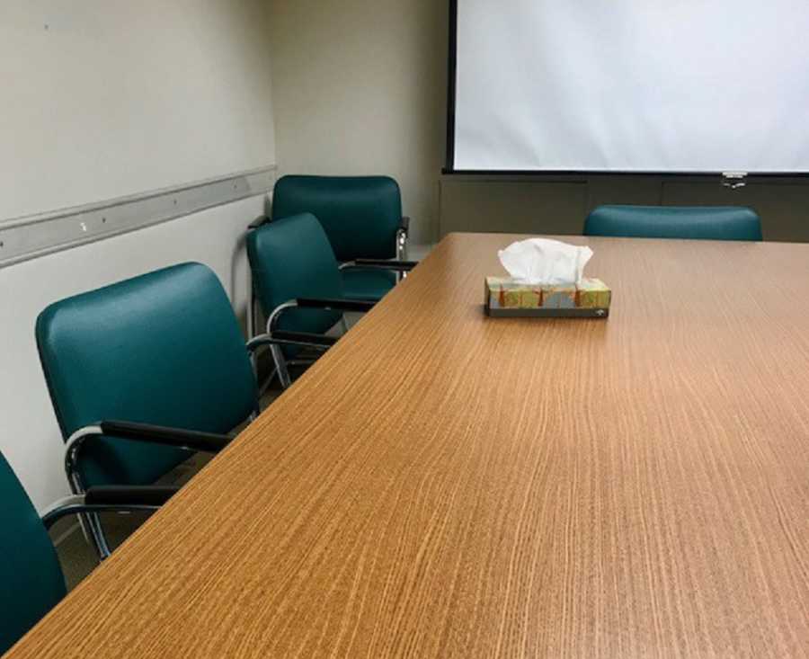 Mom snaps photo of conference room with green chairs and a box of tissues on the table