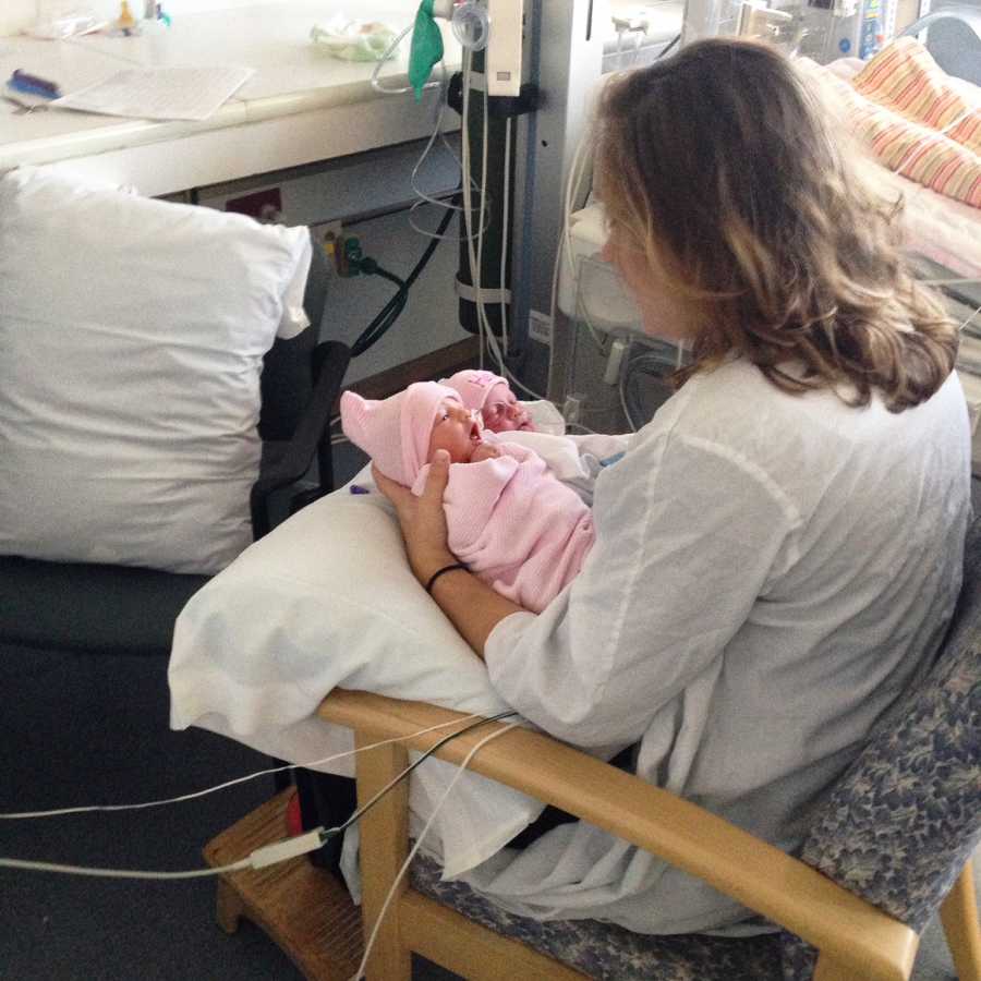College student who only ever wanted to be a mother sits in hospital chair holding her newborn twin girls