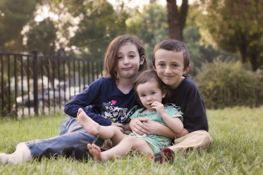 Boy whose mother had him at seventeen sits in grass with two little sisters
