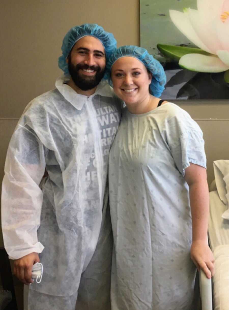 Husband without sperm and wife stand smiling in scrubs before egg retrieval