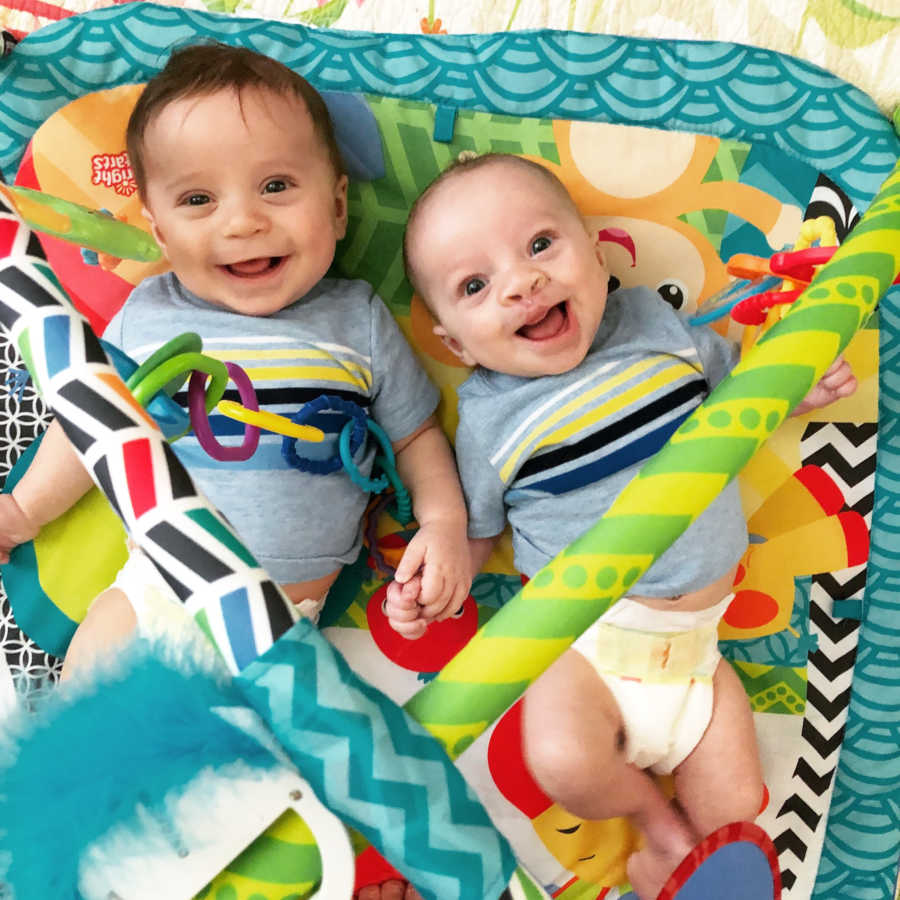 Twin brothers, one of which has cleft pallet, lay on play mat smiling