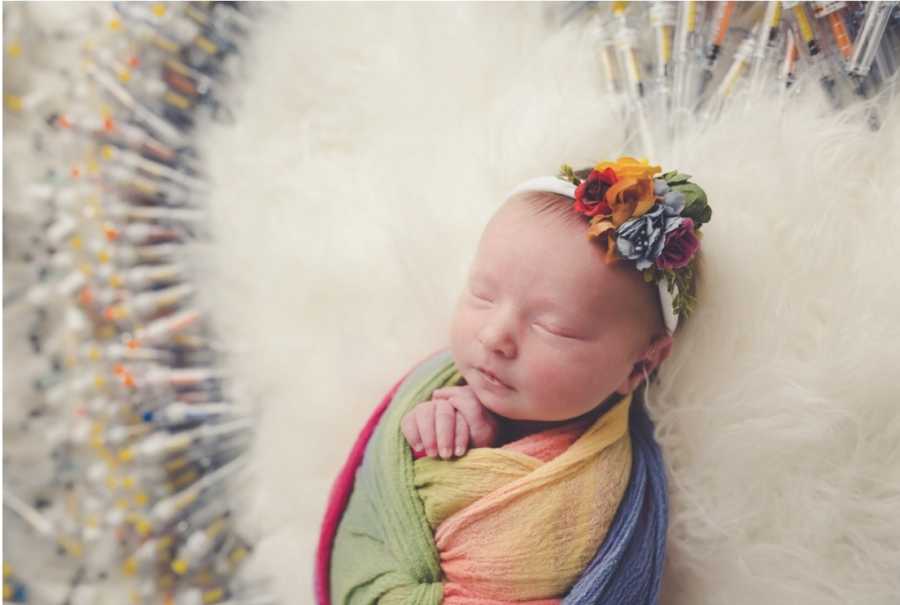 Close up of newborn swaddled in rainbow blanket with IVF needles surrounding her