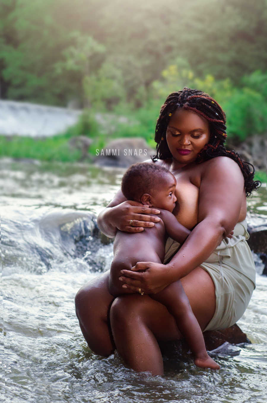 Mother sits on rock in river breastfeeding her son