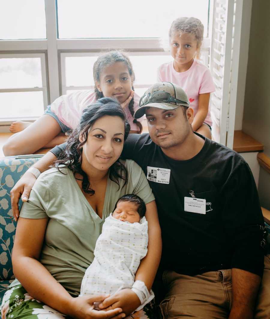 Mother who struggled to have third child sits with husband holding newborn with two daughter behind them