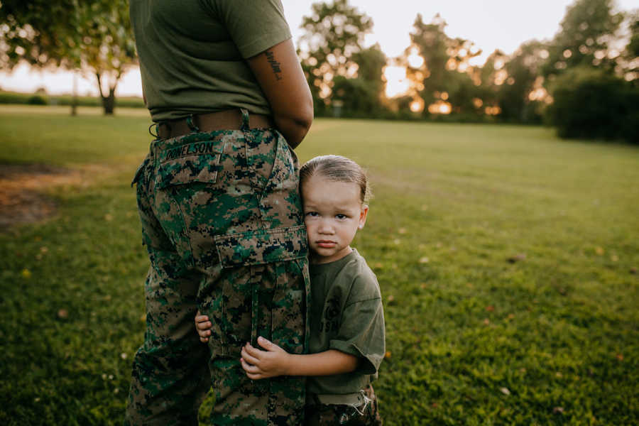 Young daughter hugs her mom's leg while they wear matching army greens