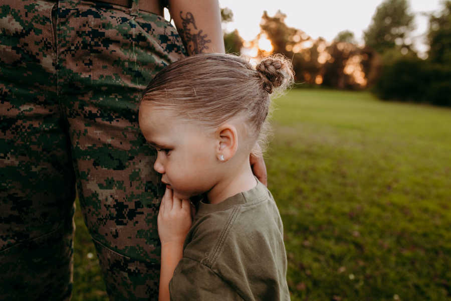 Daughter looks sad while hugging marine mom's leg during photoshoot