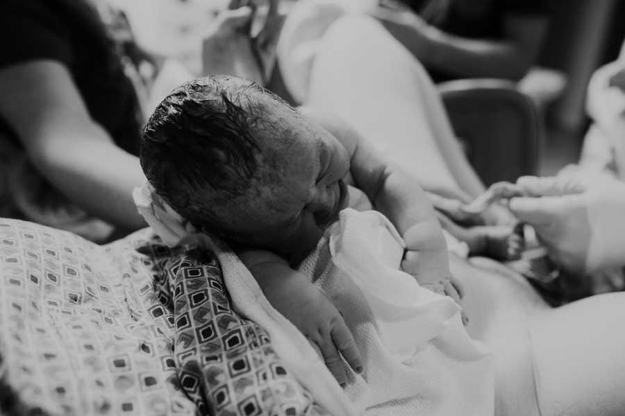 Newborn baby cries while being passed to their mom after being born