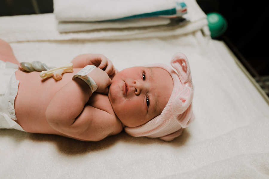 Newborn daughter lays in the hospital after birth with pink bow on her head