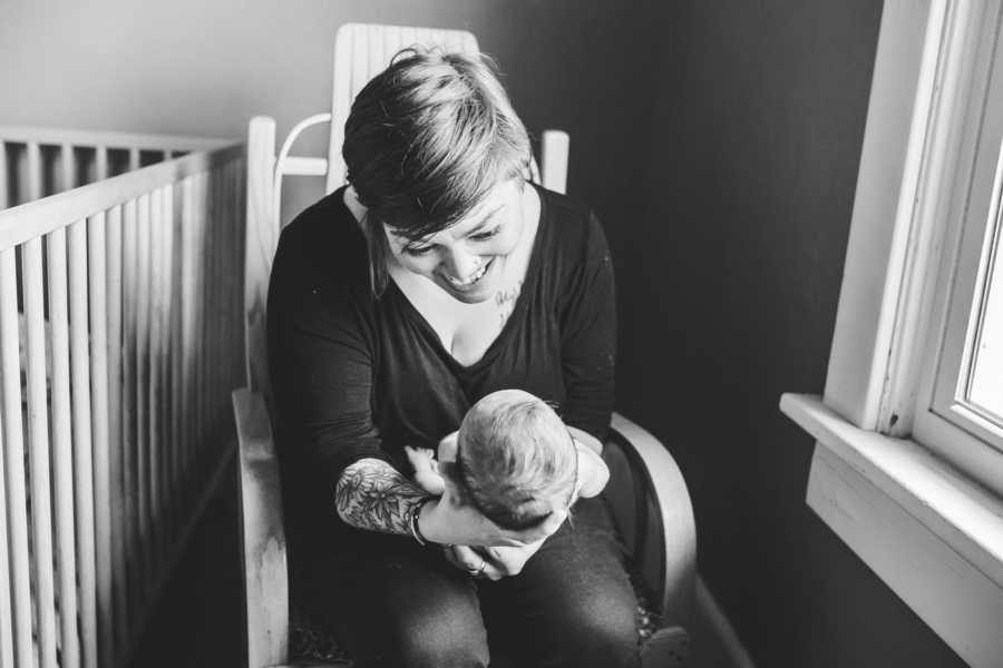 Foster mother sit in rocking chair holding newborn beside crib