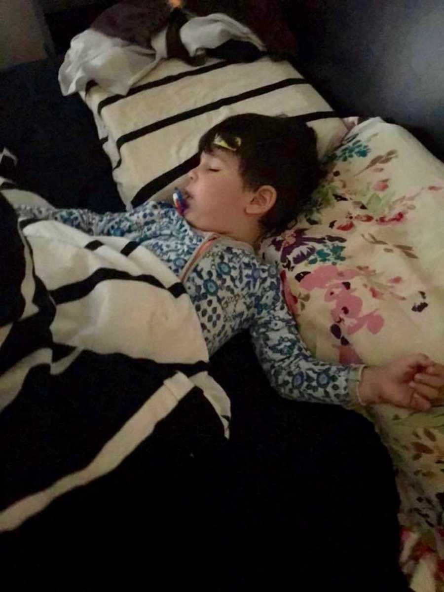 Mom takes a photo of her toddler son sleeping in bed in a blue onesie