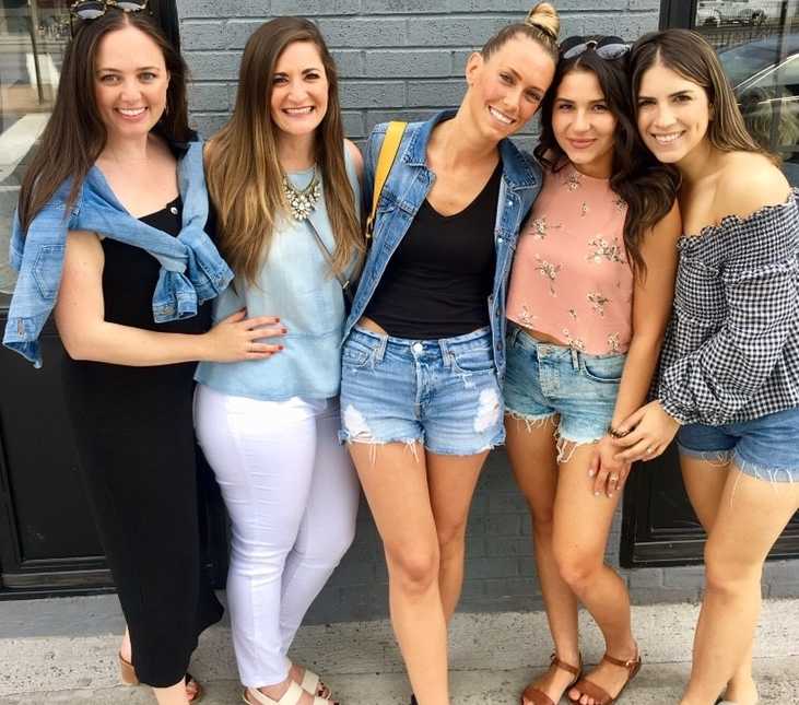 Group of women take a photo together while standing in front of a gray brick wall